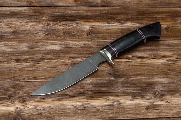Jagdmesser aus Stahl handgefertigt auf braunem Holzhintergrund, Nahaufnahme