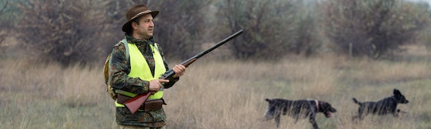 Jagdzeit Herbstsaison offen Ein Jäger mit Gewehr in der Hand in Jagdkleidung im Herbstwald auf der Suche nach einer Trophäe Ein Mann steht mit Waffen und Jagdhunden auf der Jagd nach Wild