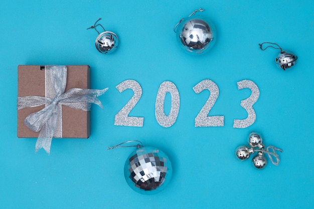 Jahr 2023 festliches Flatlay-Arrangement mit funkelnden silbernen Ornamenten und Geschenkbox auf blauem Hintergrund