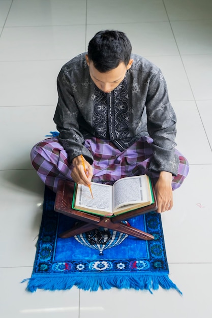 Foto jakarta indonesia 18 de abril de 2018 hombre musulmán sentado en la alfombra mientras lee el corán durante el ramadán en casa