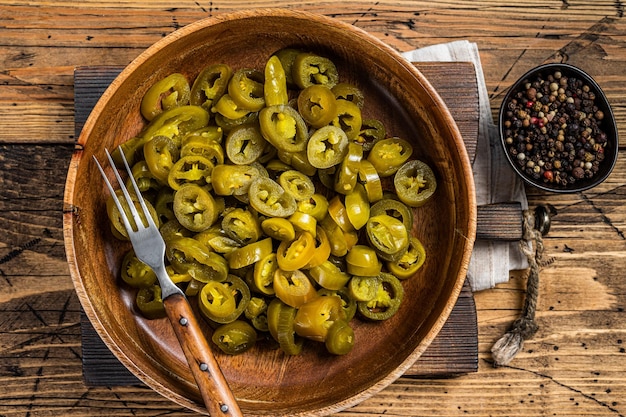 Jalapeños encurtidos y rebanados, en placa de madera vieja. Fondo de madera. Vista superior.