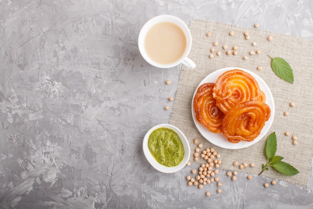 Jalebi indiano tradicional dos doces na placa branca com chutney da hortelã em um copyspace concreto cinzento. vista do topo.