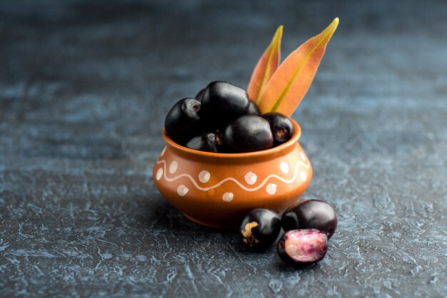 Jambolan Pflaume oder Jambul oder Jamun Frucht, Java Pflaume (Syzygium cumini) mit Blatt auf Stein strukturierte Wand.