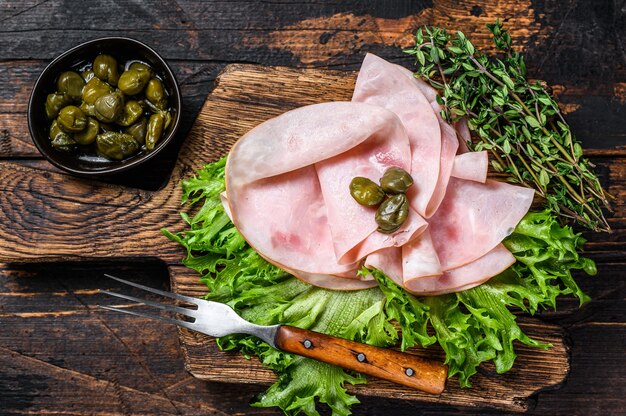 Jamón ahumado en rodajas con ensalada fresca y hierbas sobre mesa de madera. Vista superior.