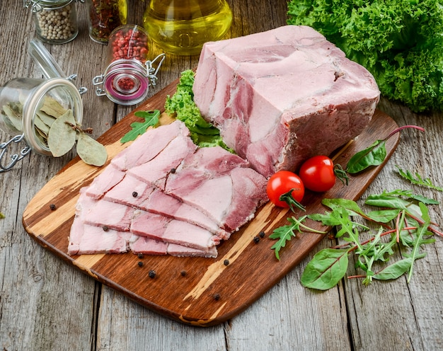 Jamón de cerdo asado con cuchillo de cocina y verduras asadas en madera rústica oscura