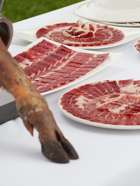 Jamón ibérico de bellota recién cortado servido en platos como aperitivo Pata de jamón de cerdo en primer plano sobre la mesa Tapas españolas para eventos o celebraciones