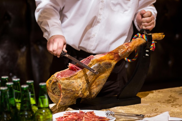 Foto jamon jamon serrano presunto espanhol tradicional em preto close-up fatiar hamon ibericoo garçom está cortando o jamon presunto inteiro em um suporte de madeira fatias de presunto parma presunto iberico presunto gourmet