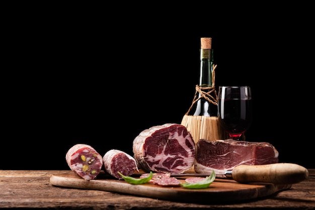 Jamón de Parma, salami de cerdo, comida de producción italiana sobre una mesa de madera sobre un fondo negro