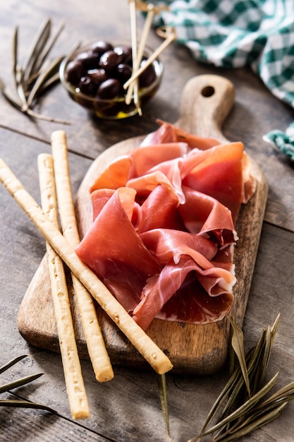 Jamón serrano español con aceitunas y palitos de pan sobre fondo de mesa de madera