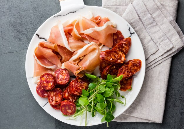 Jamón serrano español y salami en plato de mármol blanco