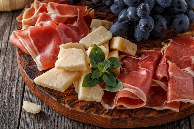 Jamón, vino, uva, parmesano en mesa de madera.