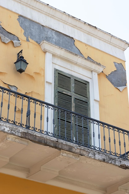 Janela branca e cáqui de um edifício amarelo descascando gesso nas paredes, varandas e balaustradas