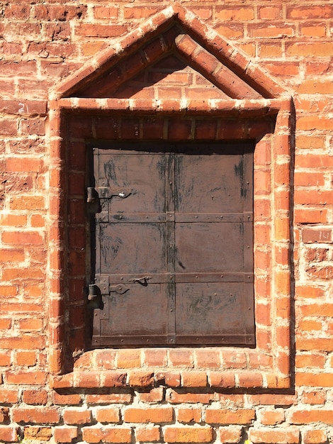 janela de igreja antiga fechada com veneziana de metal surrada em moldura de pedra