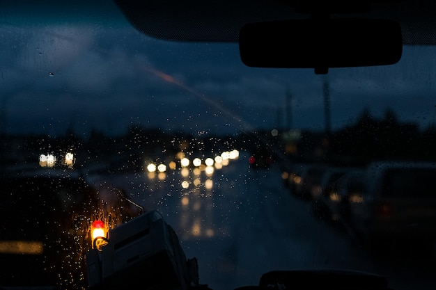 Janela dianteira do carro com pingos de chuva e estrada com carros à noite