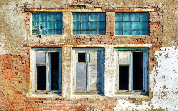 Janelas quebradas danificadas pelo grunge na parede de construção arruinada de tijolos