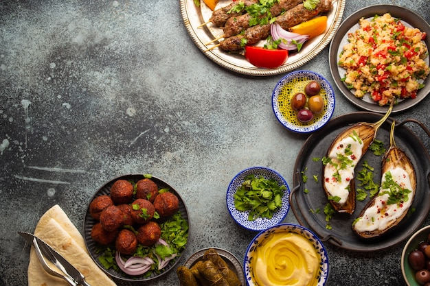 Jantar do Oriente Médio ou Mediterrâneo com kebab grelhado, falafel, verduras assadas e frescas, meze árabe variado e petiscos em mesa rústica de fundo. Sobrecarga da mesa de jantar, espaço para texto