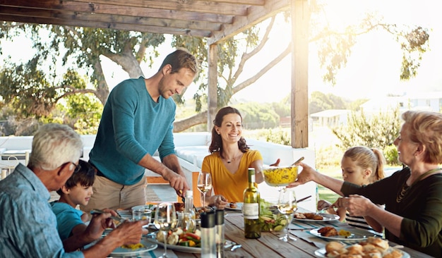 Jantar feliz em família e almoço com ligação ao ar livre no pátio com conversação relaxar ou hospedar comida saudável pais avós e crianças na mesa de jantar no quintal de casa com conversa e diversão