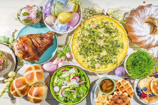 Jantar festivo, brunch de Páscoa. Pratos tradicionais de Páscoa na mesa da casa da família - carne assada, quiche, salada primavera, muffin, ovos coloridos, pãezinhos quentes