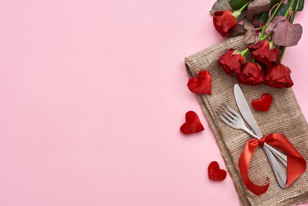 Jantar romântico perto do cenário da mesa com rosas vermelhas frescas e corações decorativos