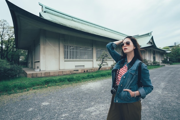 japan reisen touristische frau im urlaub, die das osaka-schloss besucht, das foto mit der kamera macht. Elegante selbstbewusste asiatische Rucksacktouristin Hand in der Tasche, die im Freien durch ein weißes altes Holzhaus mit grünem Dach steht