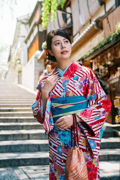 Japanische Dame mit buntem Kimono, die die Treppe hinuntergeht, mit vielen japanischen Holzgebäuden im Hintergrund. asiatischer Tourist, der in Kyoto einen Sommerkimono anprobiert. reisende reisen im sommer in japan.