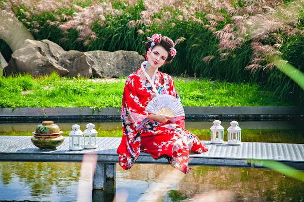 Japanische Geisha-Frau mit ausgefallenem Make-up im Garten mit einem Ventilator