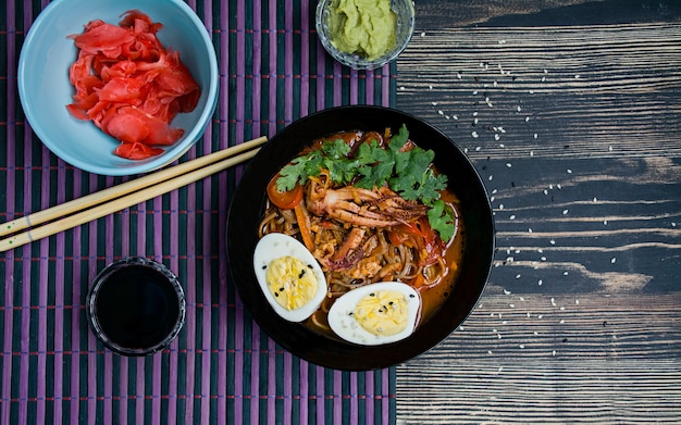 Japanische ramen mit meeresfrüchten, kräutern und in essig eingelegten eiern auf einer dunklen oberfläche