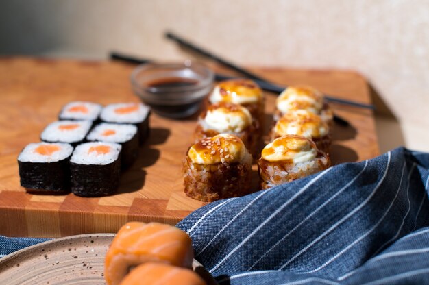Japanische Sushirollen dienten auf hölzernem Hintergrund. Sushi-Rollen Philadelphia, heiß gebratene Rolle mit Sahne, Maki, Essstäbchen und Sojasauce
