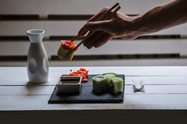 Foto japanische traditionelle rollen, die in einer sushi-bar auf einem weißen tisch serviert werden. nahaufnahme der männlichen hand mit einem stück rolle