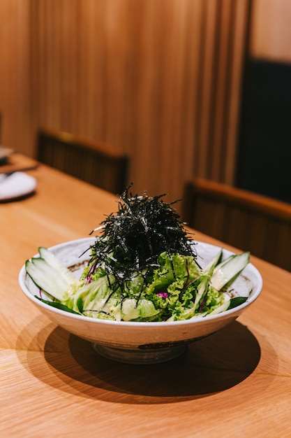 Japanischer Gurkensalat mit Kopfsalat, Rettich und trockener Meerespflanze diente in einer keramischen Schüssel auf dem hölzernen Zähler.