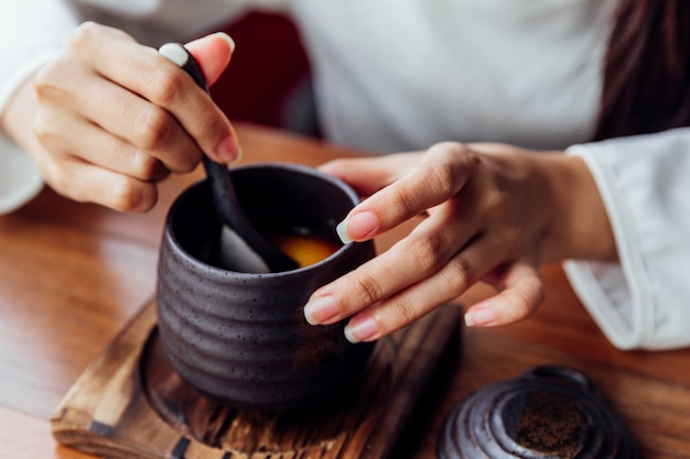 Japanischer Karamellpudding diente in einer schwarzen Keramikschale, die mit weiblicher Hand weichen Pudding schöpft