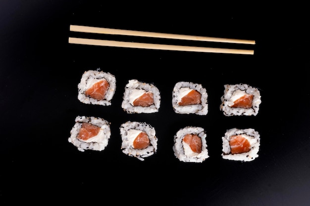 Japanisches Essen mit vier nebeneinander liegenden Lachs-Sushi-Rollen und Frischkäse und Essstäbchen in Draufsicht