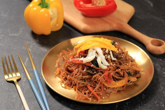 Japchae coreano, fideos de vidrio salteados, carne de res y verduras, servido en plato dorado. Comida popular para Seollal