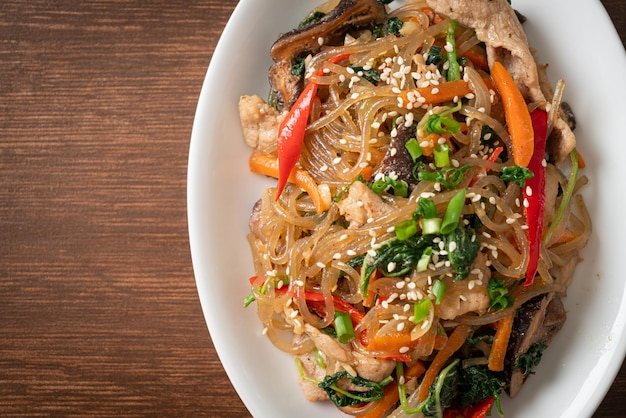 japchae o fideos de fideos coreanos salteados con verduras y carne de cerdo cubiertos con sésamo blanco - estilo de comida tradicional coreana