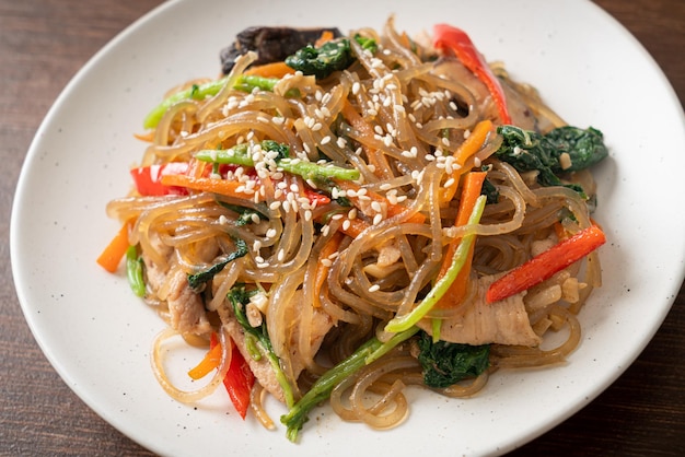 japchae o fideos de fideos coreanos salteados con verduras y carne de cerdo cubiertos con sésamo blanco - estilo de comida tradicional coreana