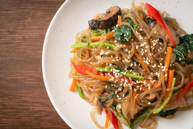 Japchae o fideos vermicelli coreanos salteados con verduras y cerdo cubiertos con sésamo blanco - estilo de comida tradicional coreana