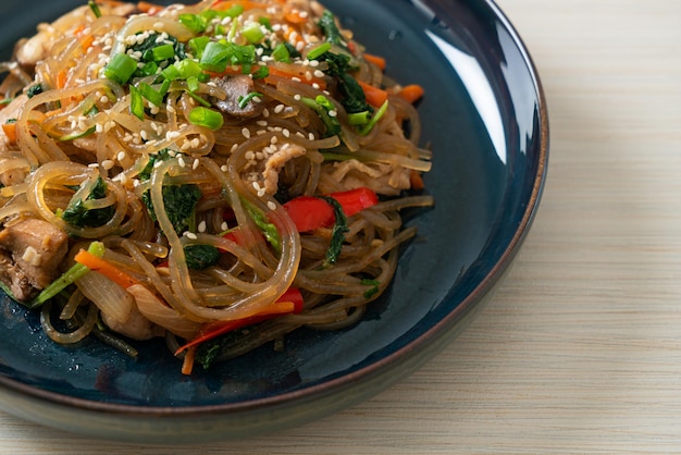 Japchae o fideos vermicelli coreanos salteados con verduras y cerdo cubiertos con sésamo blanco