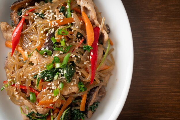 Japchae oder gebratene koreanische Fadennudeln mit Gemüse und Schweinefleisch, garniert mit weißem Sesam - traditionelle koreanische Küche