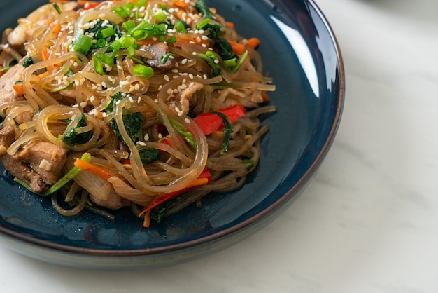 Japchae oder gebratene koreanische Vermicelli-Nudeln mit Gemüse und Schweinefleisch mit weißem Sesam