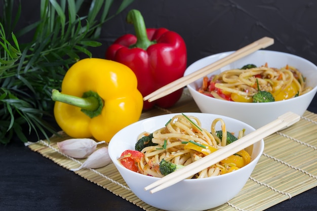 Japonés dos tazones de fideos salteados con verduras, salsa de soja y pimientos sobre una estera de bambú