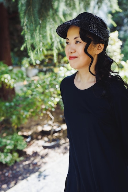 Japonesa de meia idade no parque de verão com chapéu de palha preta