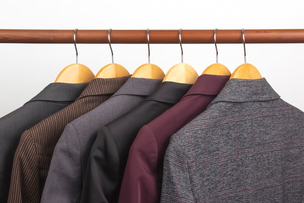 Jaquetas clássicas de escritório para mulheres diferentes estão penduradas em um cabide para guardar roupas. A escolha do estilo de roupas da moda