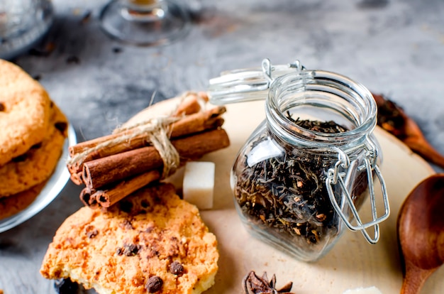 Jar com chá, biscoitos caseiros e especiarias para chá em fundo escuro