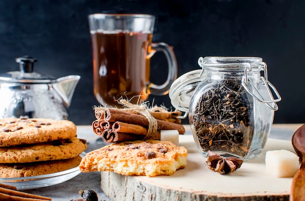 Jar com chá, biscoitos caseiros e especiarias para chá em fundo escuro,