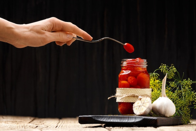 Jar com conservas de tomate em um fundo de madeira um tomate em um garfo