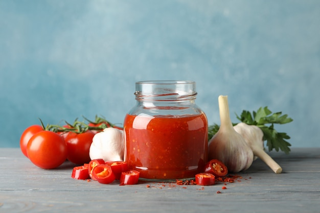 Jar com pimenta vermelha e molho de tomate e especiarias na mesa de madeira