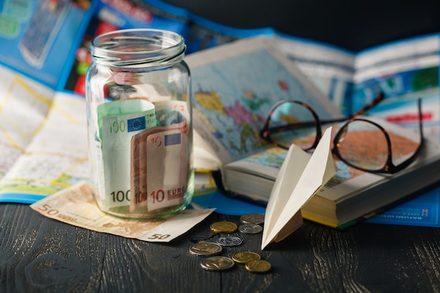 Jar con dinero para un viaje, avión, mapas, pasaporte y otras cosas para la aventura.