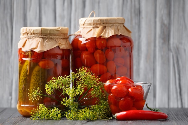 Jar con pepinos enlatados y tomates cereza en un fondo de madera