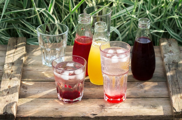 Jarabes de fresa, cereza y ruibarbo y vasos con agua en una mesa de madera en el jardín.