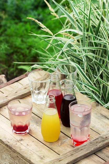 Jarabes de fresa, cereza y ruibarbo y vasos con agua en una mesa de madera en el jardín.